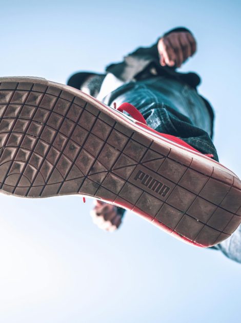 Low angle view of person wearing sneakers with focus on the sole against blue sky.