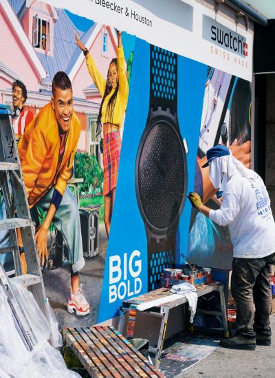 A street artist creates a vibrant mural in an urban setting near Swatch store.