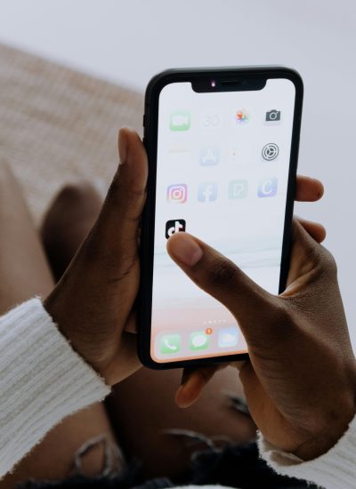 Hands holding a smartphone showing various apps including TikTok in a close-up view.