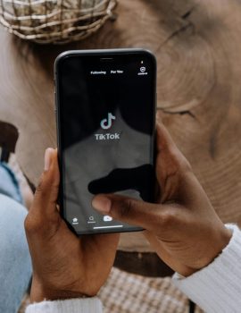 Close-up of hands holding a smartphone displaying the TikTok app interface on a wooden surface.