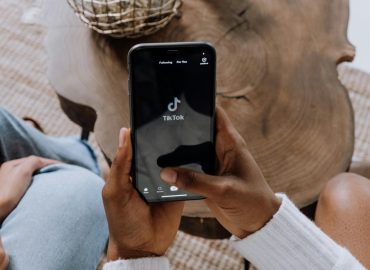 Close-up of hands holding a smartphone displaying the TikTok app interface on a wooden surface.