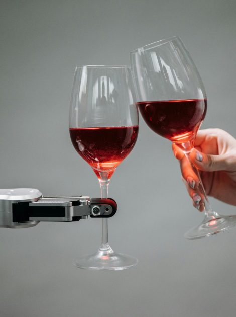 A robot and a human hand clinking glasses of red wine, symbolizing technology and celebration.